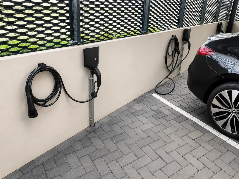 Easee-laadpaal aan de muur bij een oprit, met een geparkeerde elektrische auto