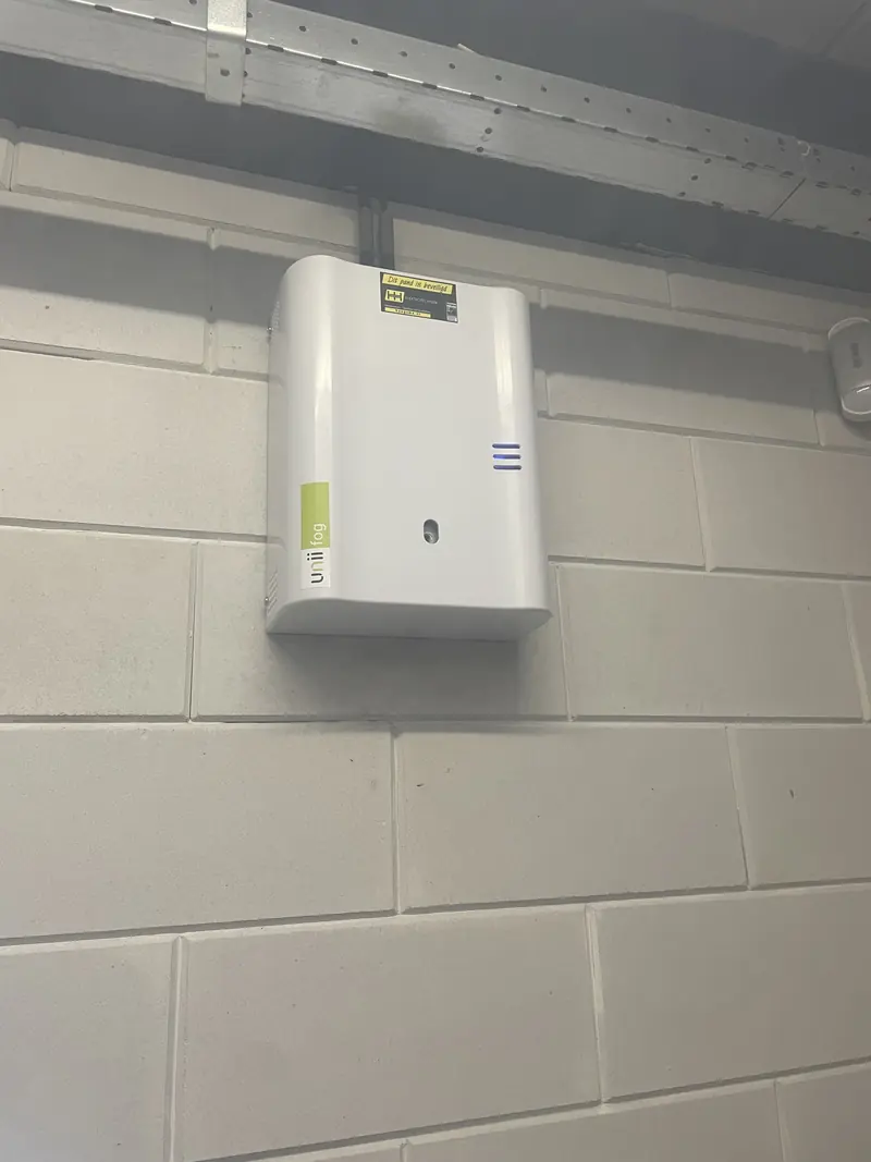 Door Haagsma geplaatste UNii-mistgenerator aan de wand, met de Haagsma-sticker en rechts een bewegingsmelder